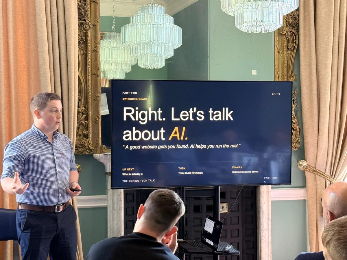 Sam presenting beside a 'Let's talk about AI' slide to a seated audience