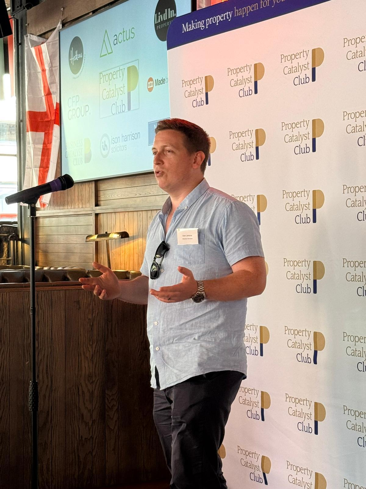 Sam speaking at the Property Catalyst Club, gesturing to the audience at the microphone