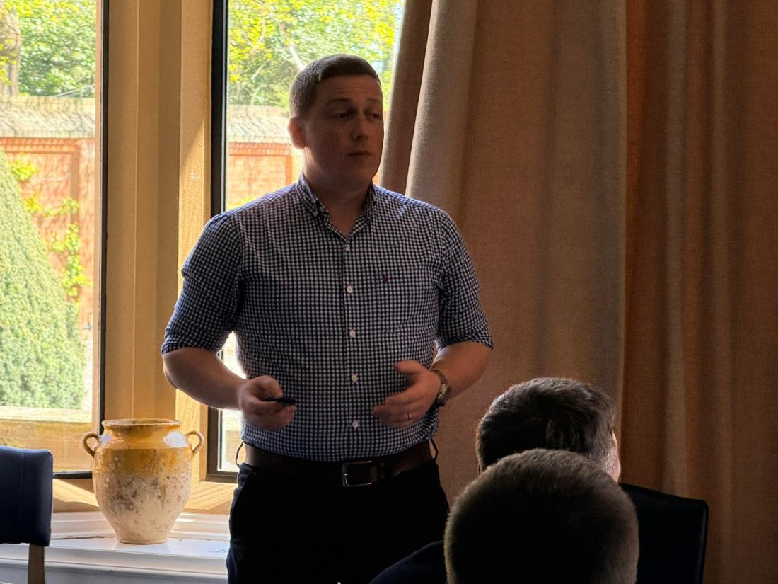 Sam mid-talk, gesturing with both hands to a room